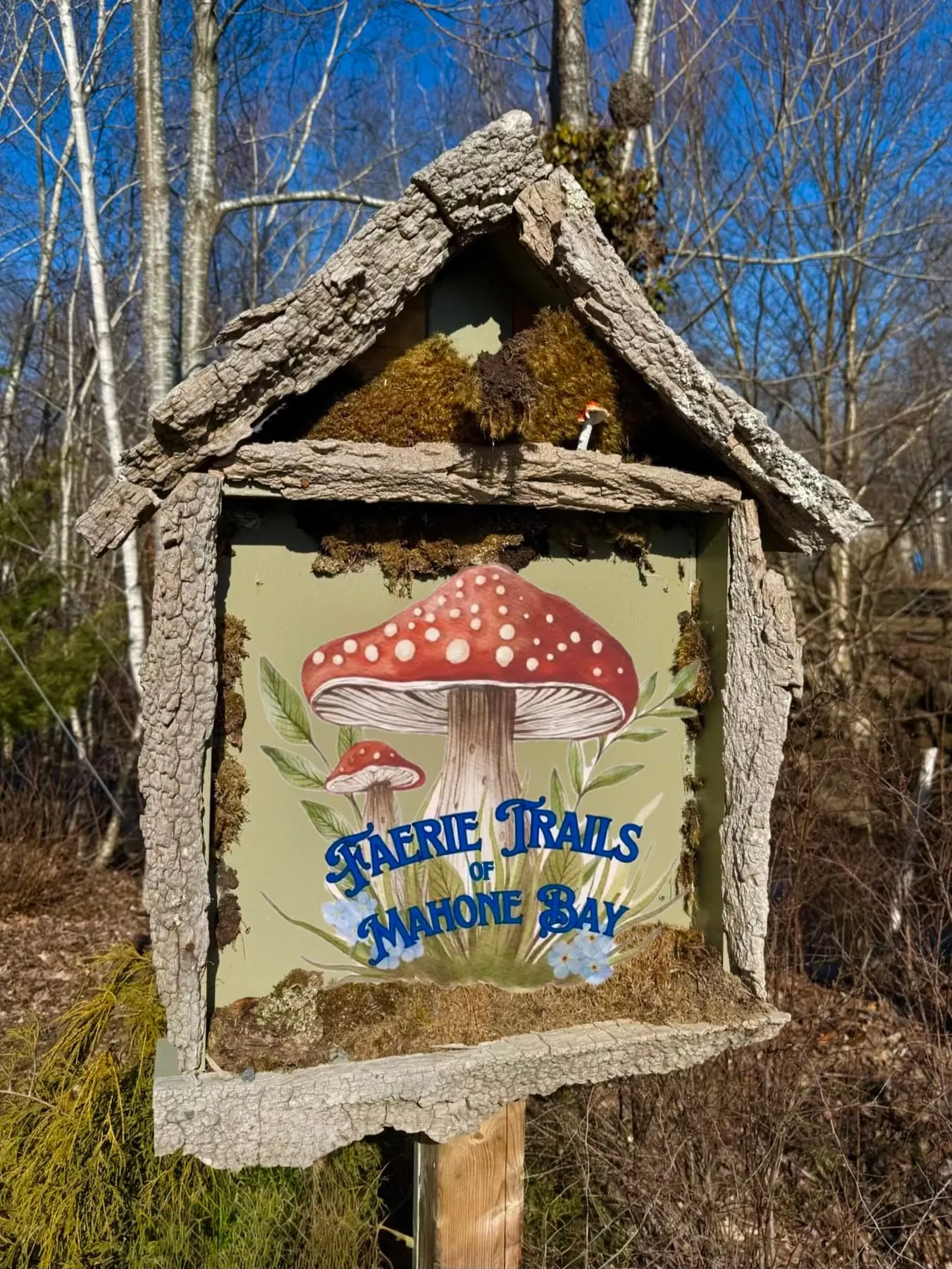 A painted Faerie Trails of Mahone Bay sign with a red toadstool at a trailhead.