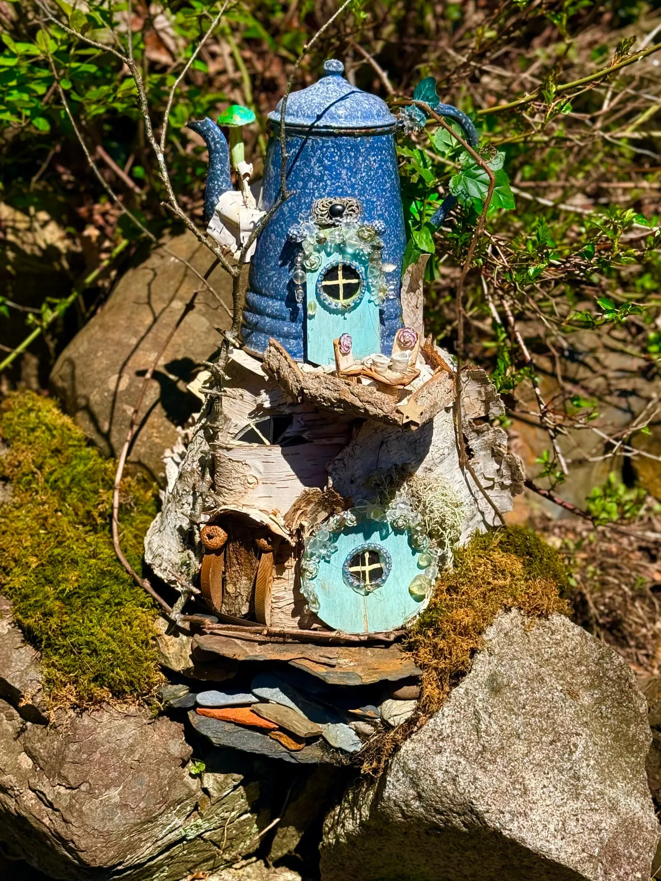 A blue faerie house with a round window, nestled in mossy bark.