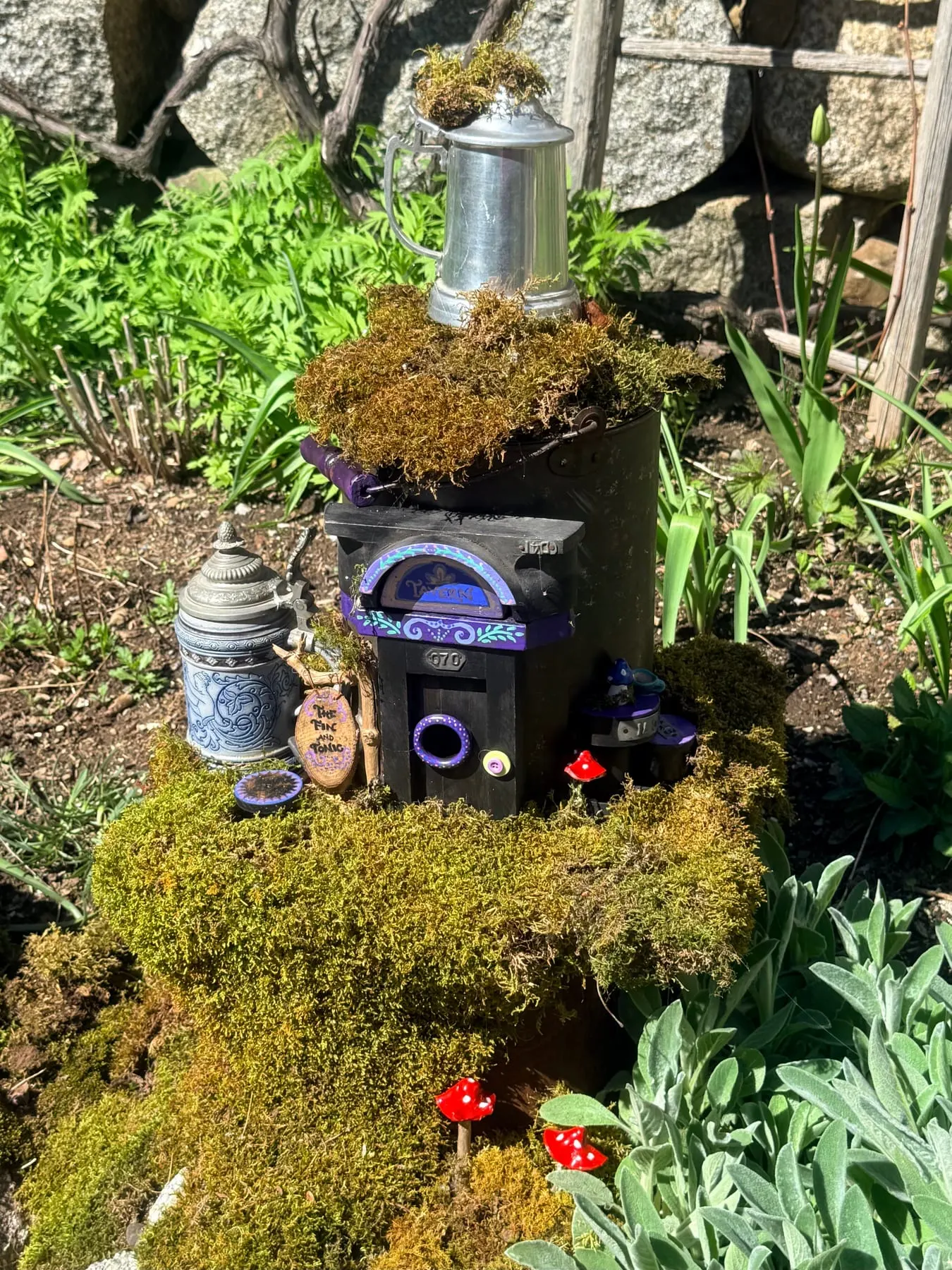 A faerie house with a round green door and a mossy roof among spring flowers.