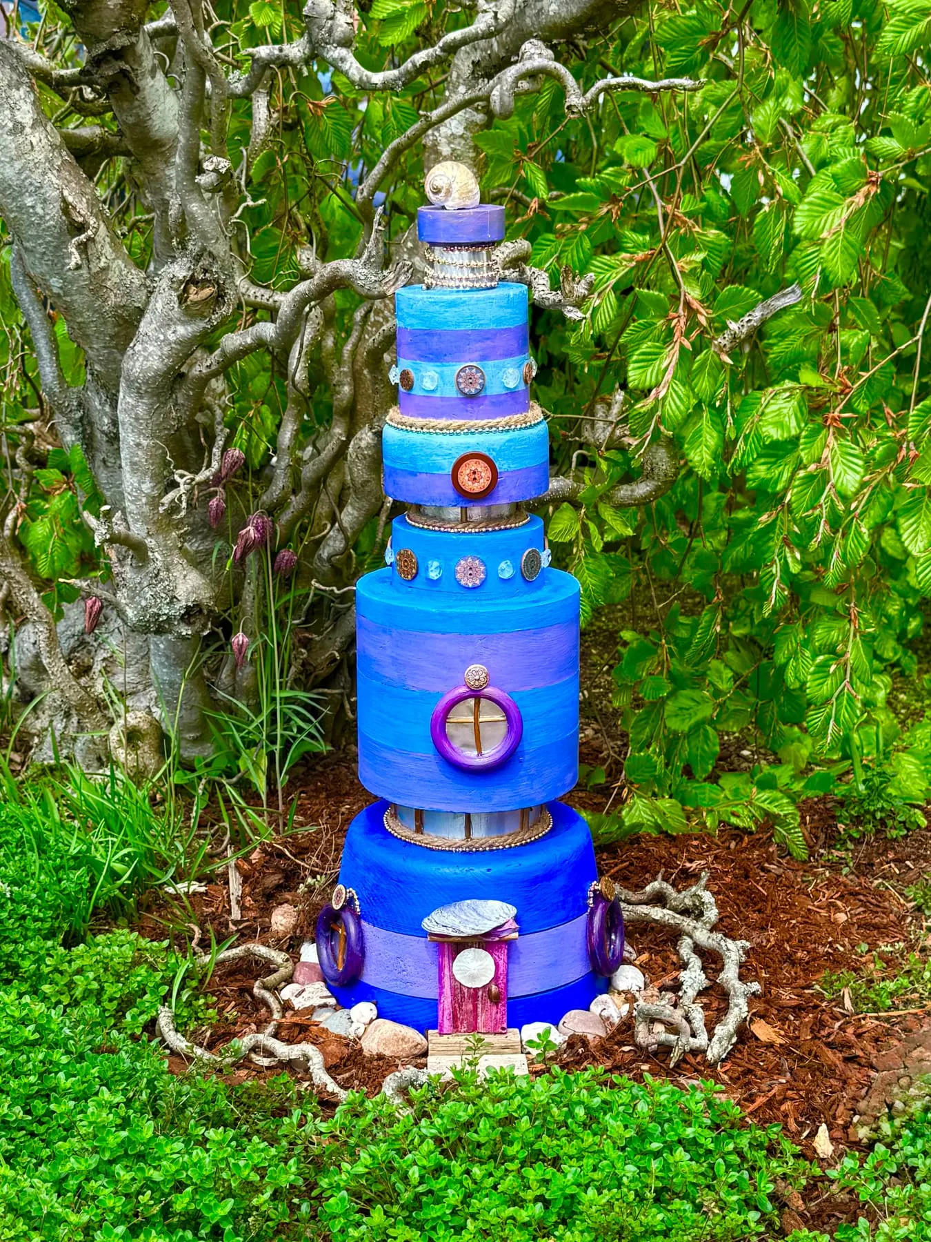 A tall blue tiered faerie tower rising from a garden stump.