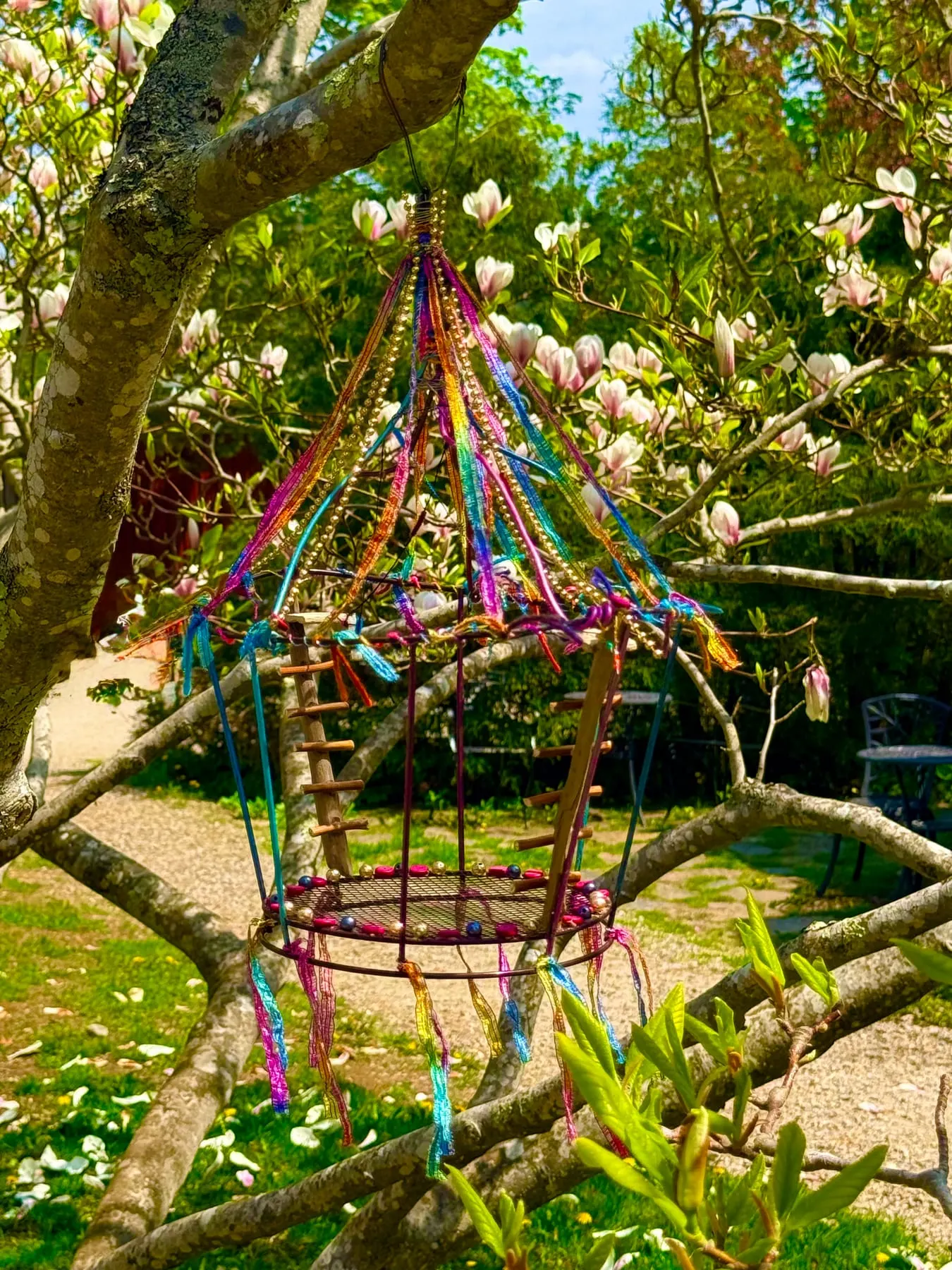 A woven willow faerie ride strung with ribbons in a sunlit garden.
