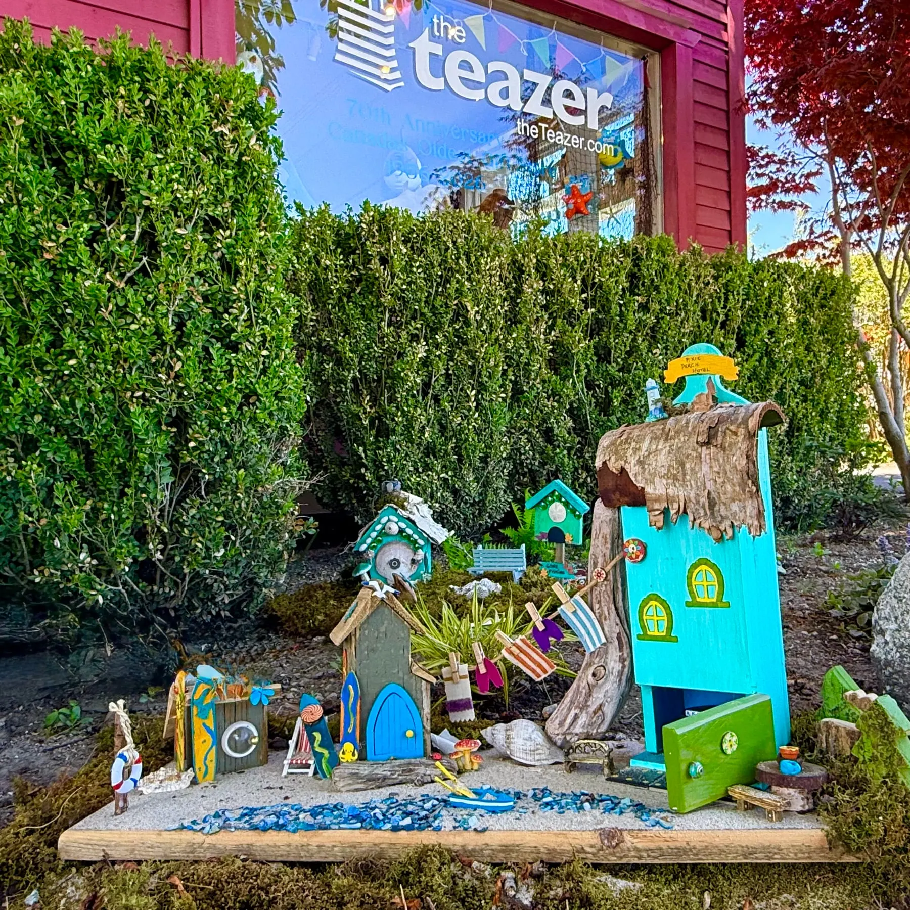 A whole cluster of colourful faerie houses with bright doors, built into a garden scene.